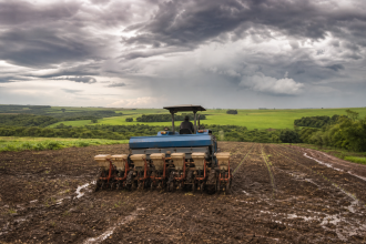 Máquina agrícola trabalha em lavoura úmida durante o início da safra brasileira de grãos.