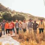 Grupo diversificado de agricultores reunido em um campo iluminado pelo sol.