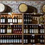 Adega rústica com garrafas de vinho alinhadas diante de uma parede de tijolos e barris de madeira.