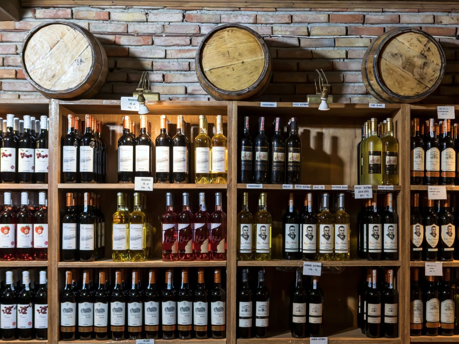 Adega rústica com garrafas de vinho alinhadas diante de uma parede de tijolos e barris de madeira.