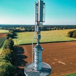 Vista aérea de uma torre de comunicação celular entre áreas agrícolas verdes.