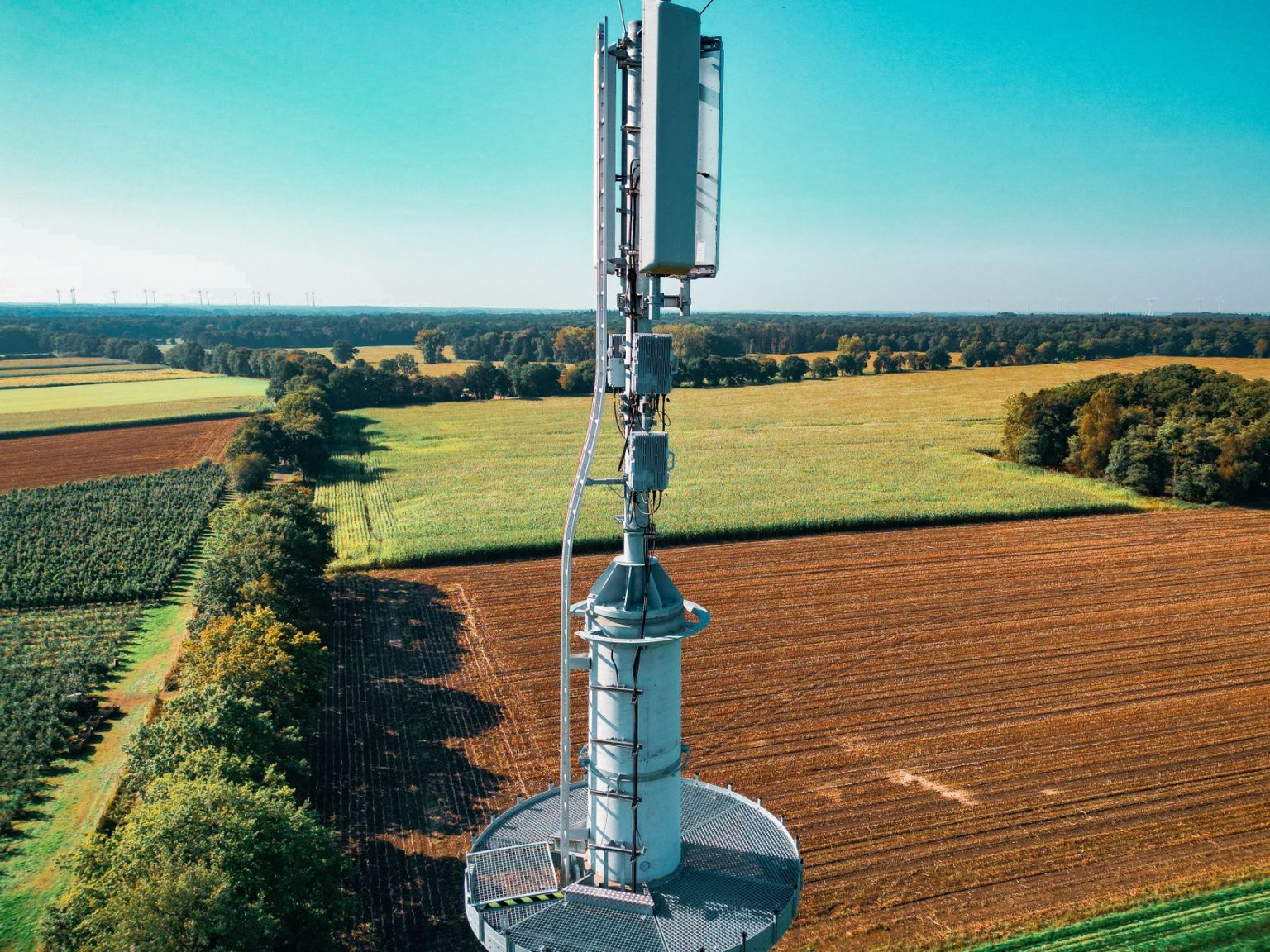 Vista aérea de uma torre de comunicação celular entre áreas agrícolas verdes.