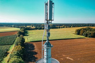 Vista aérea de uma torre de comunicação celular entre áreas agrícolas verdes.