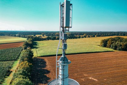 Vista aérea de uma torre de comunicação celular entre áreas agrícolas verdes.