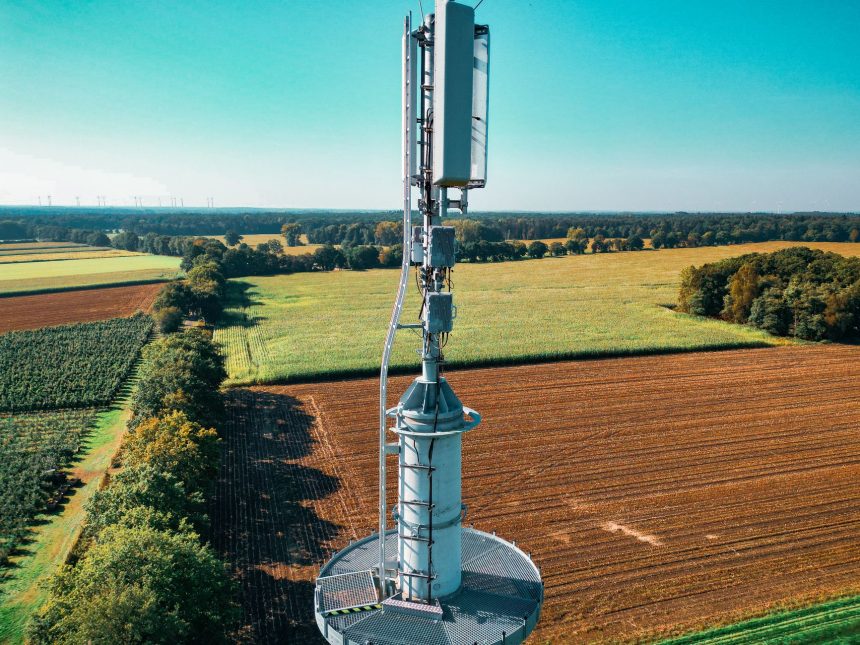 Vista aérea de uma torre de comunicação celular entre áreas agrícolas verdes.